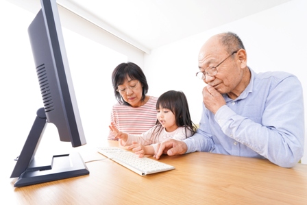 An Asian grandfather sits before a computer screen with his two grandchildren