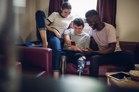 Three teens, one an amputee, sitting in a living room watching a screen