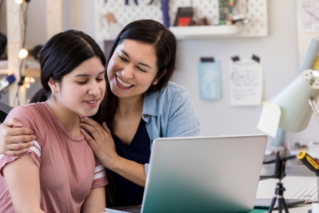 A mother comforts her daughter while both look at a computer screen