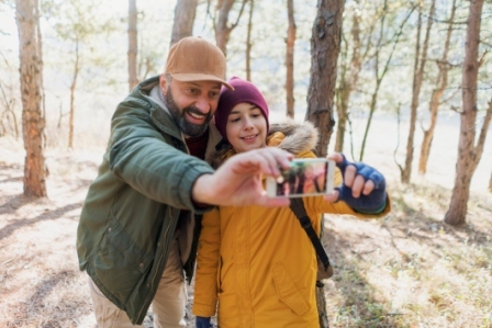 A father and son outdoors in the woods, smiling taking a selfie