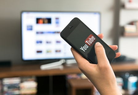 A photo of a hand with a photo with YouTube on it, as the person sits in front of a television
