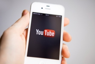 A hand holds a smartphone with YouTube on the screen