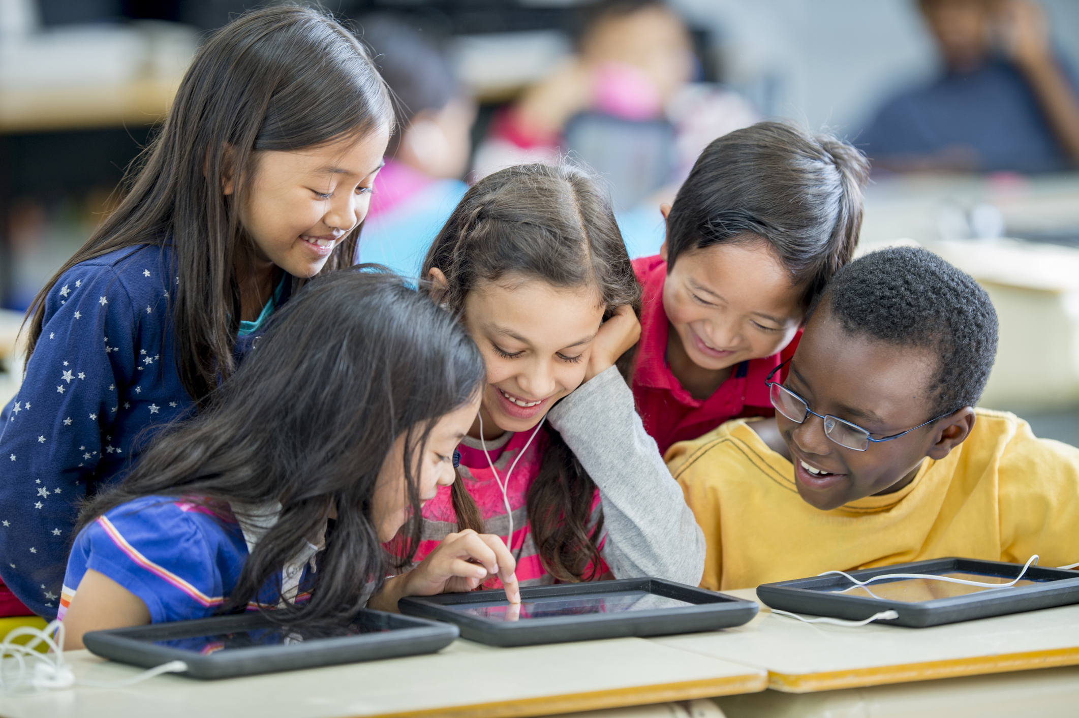 Several children in classroom looking over an ipad screen