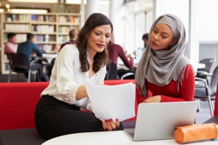 A teacher and a teenage muslim girl in a school library looking at a computer screen