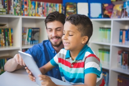 An male teacher and a young male student smile as they look at a device screen