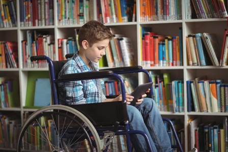 A young boy in a wheelchair looks down at the device in his hands