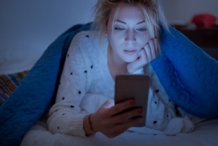 Girl in the dark under a blanket looking at phone