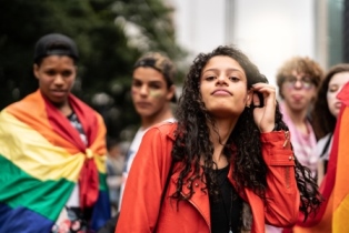 Group of varying gender teens standing with a pride flag