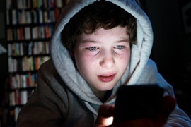 Boy wearing hoodie in dark room using mobile device