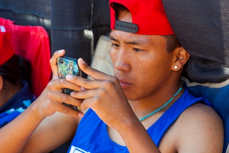An indigenous male teen looks closely at the screen of his smartphone