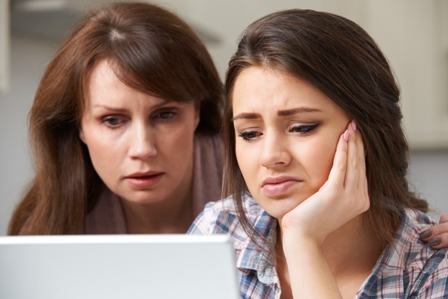 A worried teen girl and her mother look at a computer screen