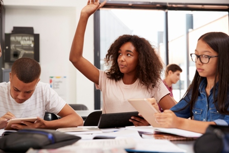 An African Amercan teenage girl raises her hand in the classroom