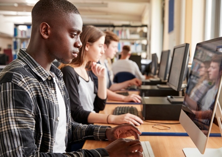 A young black man sits at a computer in a classroom setting with other students at their computers