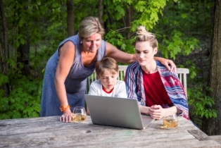 Female with two youth outdoors at picnic table looking at laptop